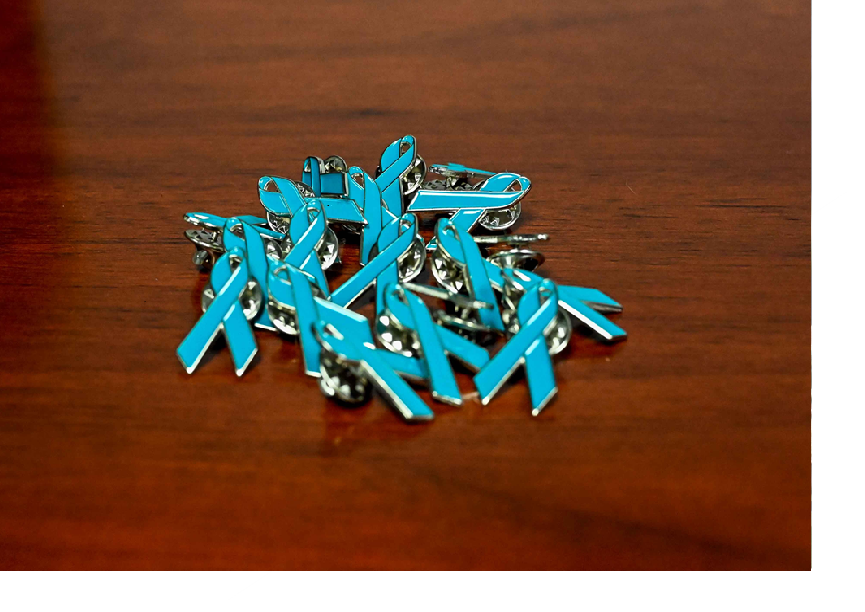 Pile of teal SAPR ribbon pins on a wood table Pile of teal SAPR ribbon pins on a wood table