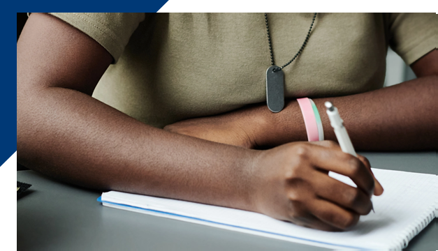 Arms of solider member sitting at a desk writing on a notepad
